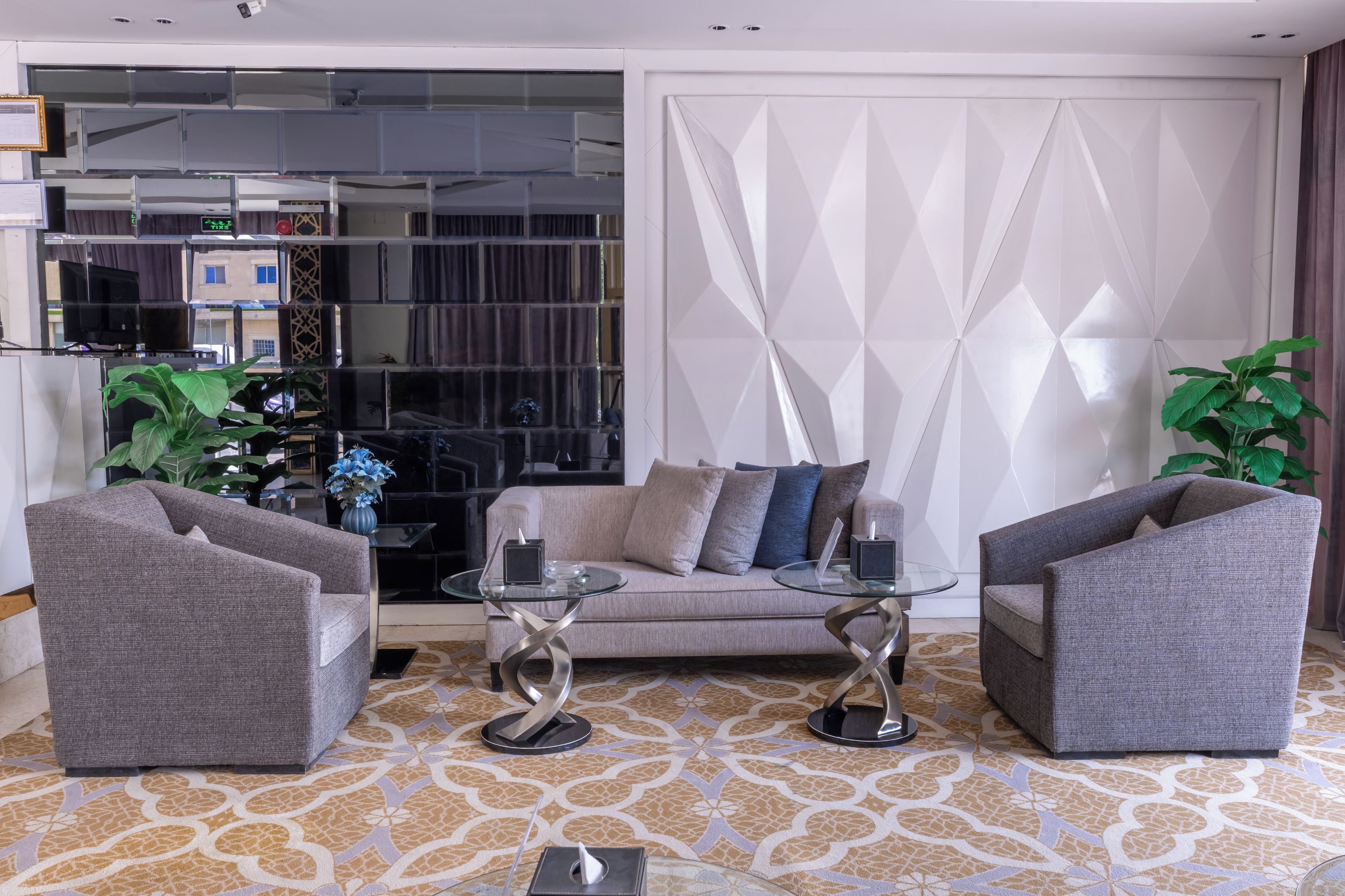 Una sala moderna con un sofá, dos sillones, una mesa de centro de vidrio y plantas decorativas.