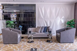 Una sala moderna con un sofá, dos sillones, una mesa de centro de vidrio y plantas decorativas.
