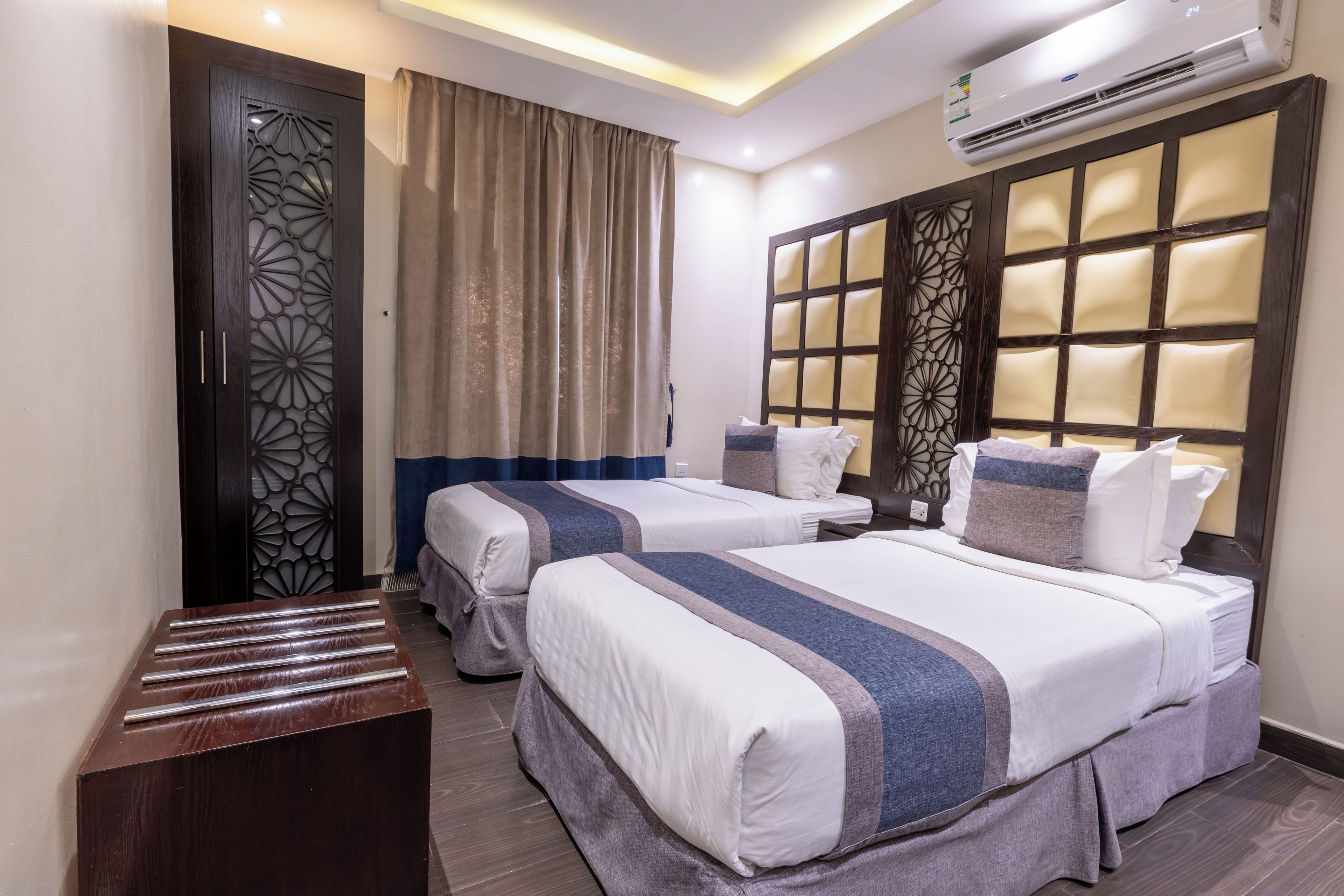A hotel room with two beds, a wardrobe, a desk, and a large window with a view.