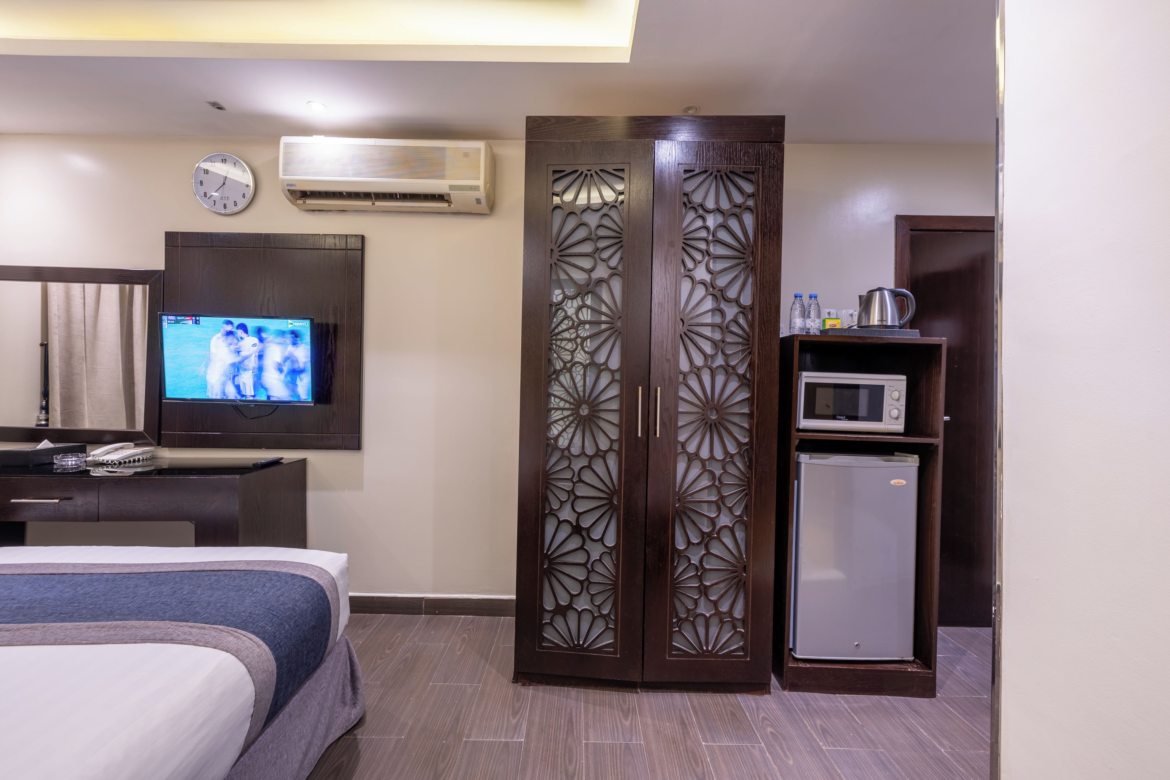 A hotel room with a bed, a television, an air conditioner, a decorative wooden partition, a microwave, and a refrigerator.