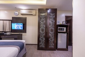 A hotel room with a bed, a television, an air conditioner, a decorative wooden partition, a microwave, and a refrigerator.