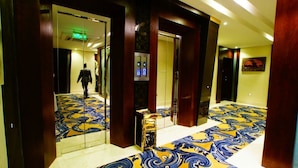 Un pasillo de hotel con alfombra estampada, un ascensor y una persona caminando.