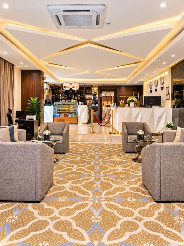 A hotel lobby with a patterned carpet, seating area, and a reception desk.