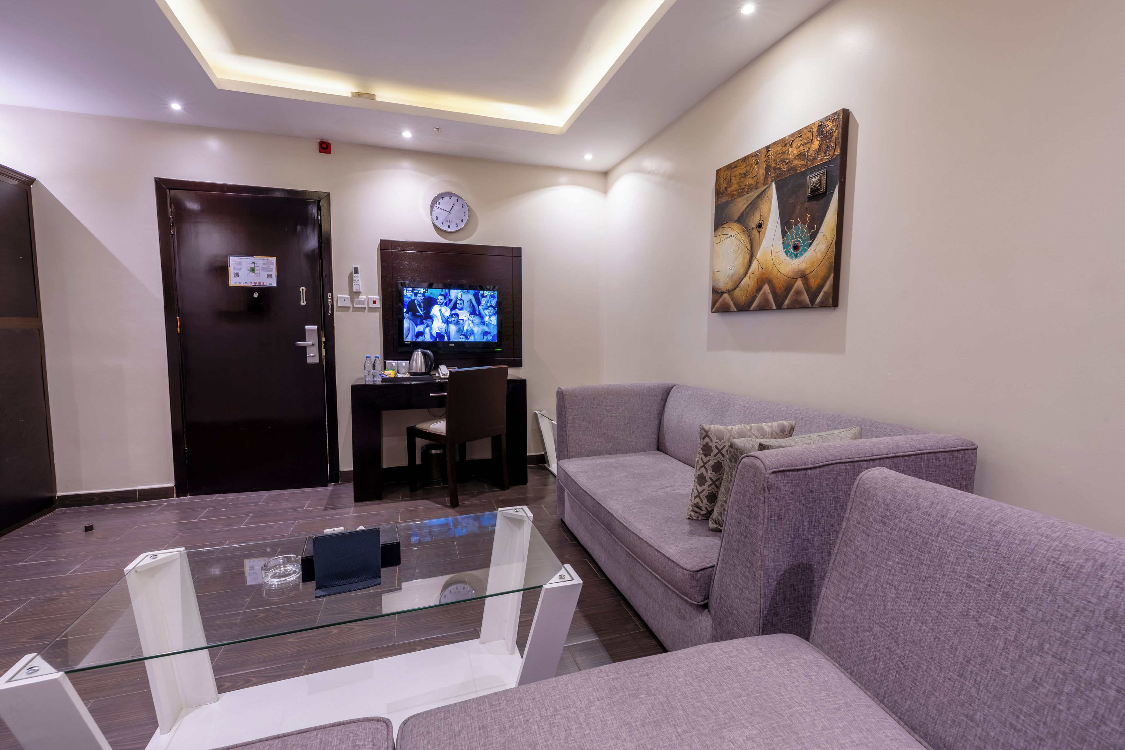 Una sala de estar moderna con un sofá, una mesa de centro de vidrio, un televisor de pantalla plana y un cuadro en la pared.