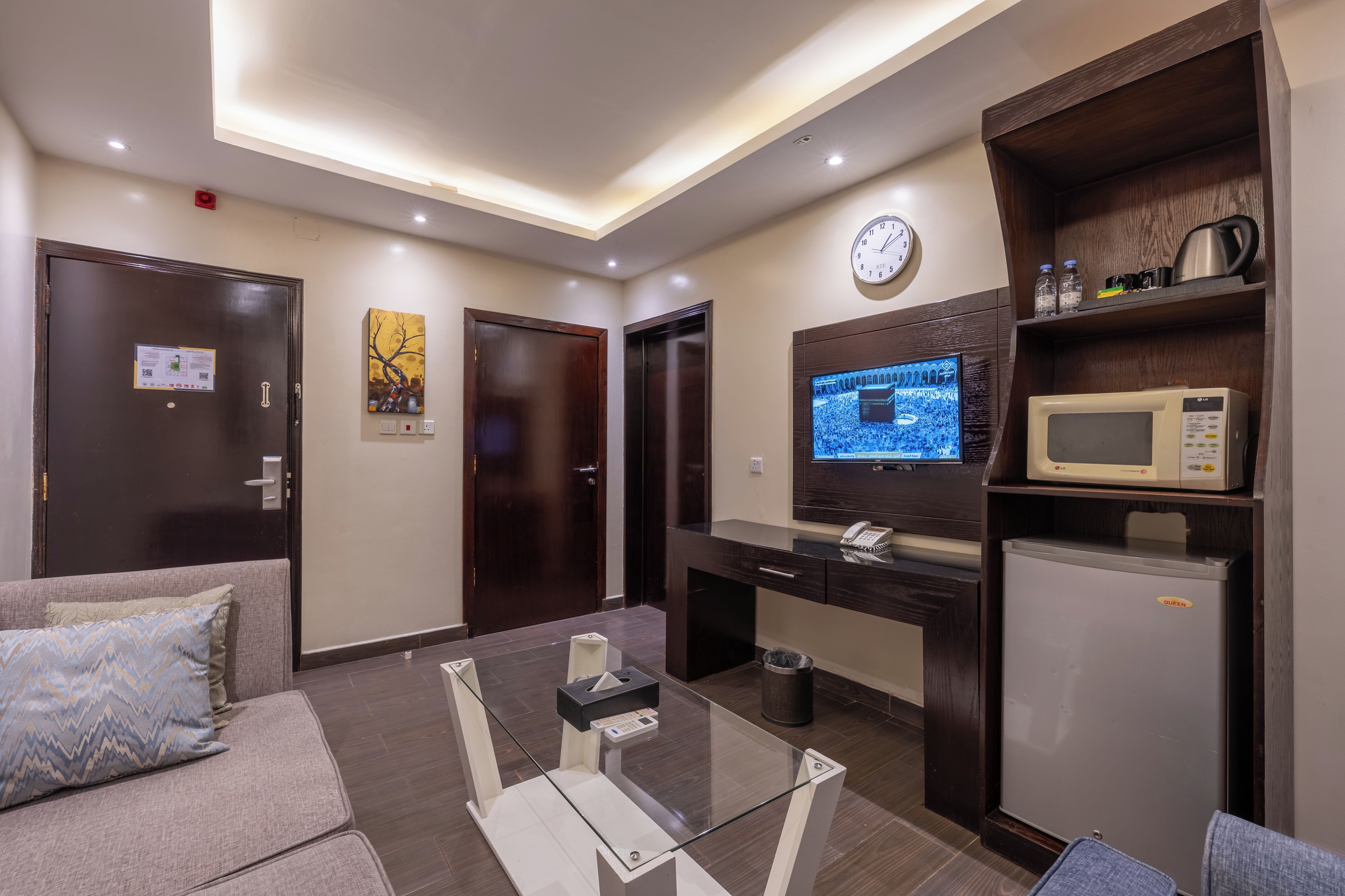 A modern living room with a sofa, a glass coffee table, a TV, a microwave, and a refrigerator.