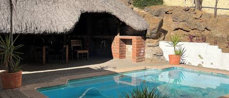 Una piscina con una estructura de techo de paja y plantas en macetas.
