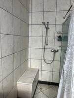 Ein Duschbereich mit Handbrause, einer festen Duschbrause und einer kleinen Ablage für Toilettenartikel.