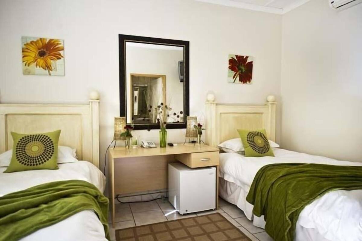 A hotel room with two beds, a desk, a mirror, and a small refrigerator.