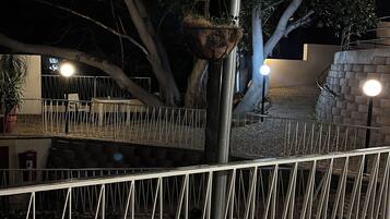 Un espacio al aire libre de noche con una pérgola de madera, barandilla metálica y pared de ladrillo.