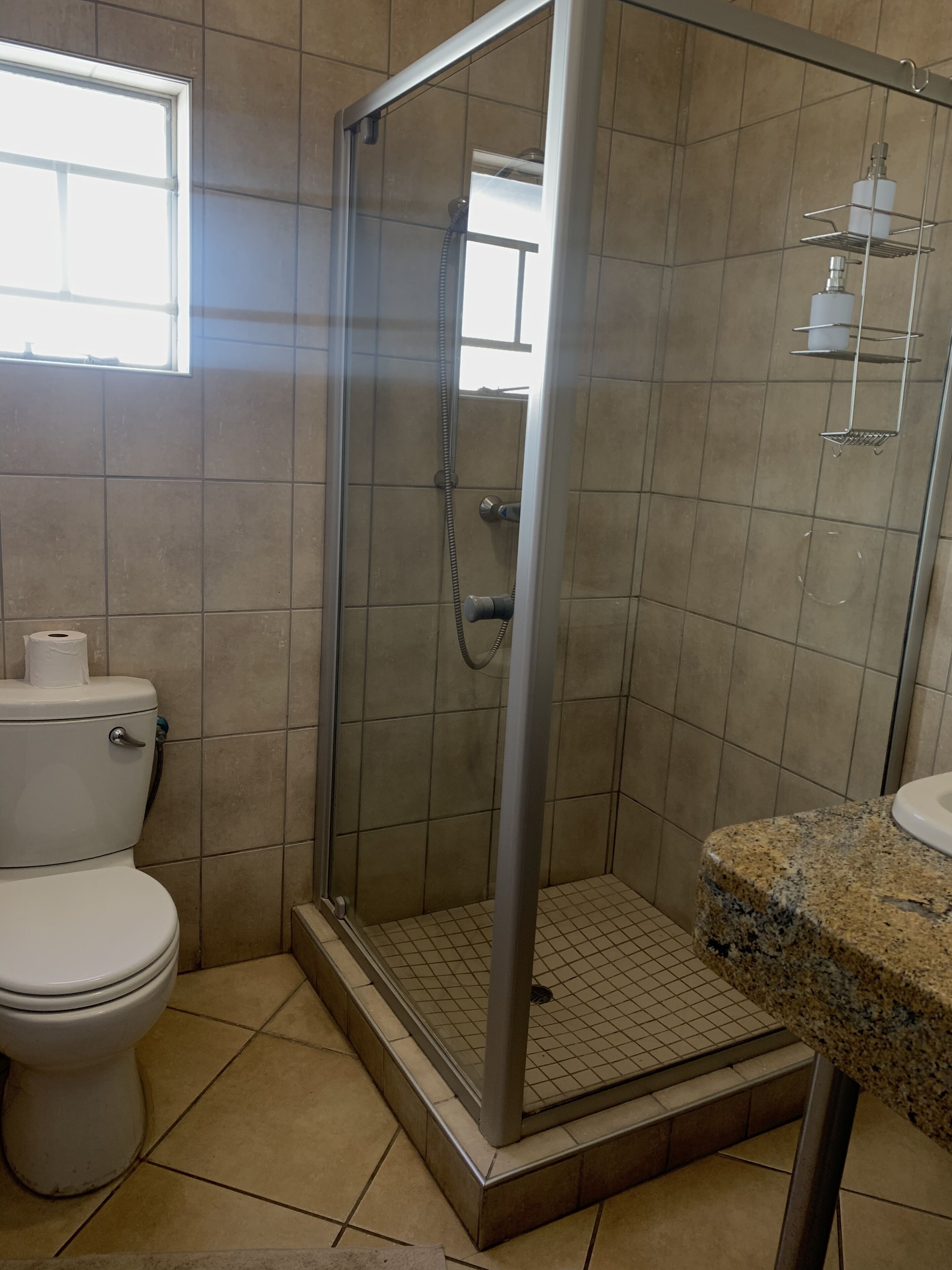 A bathroom with a glass-enclosed shower, a toilet, and a granite countertop.