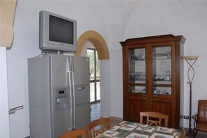 A room with a dining table, chairs, a television on a stand, a cabinet with glass doors, and a floor lamp. - Bed & Breakfast Villa Rita (Campi Salentina)