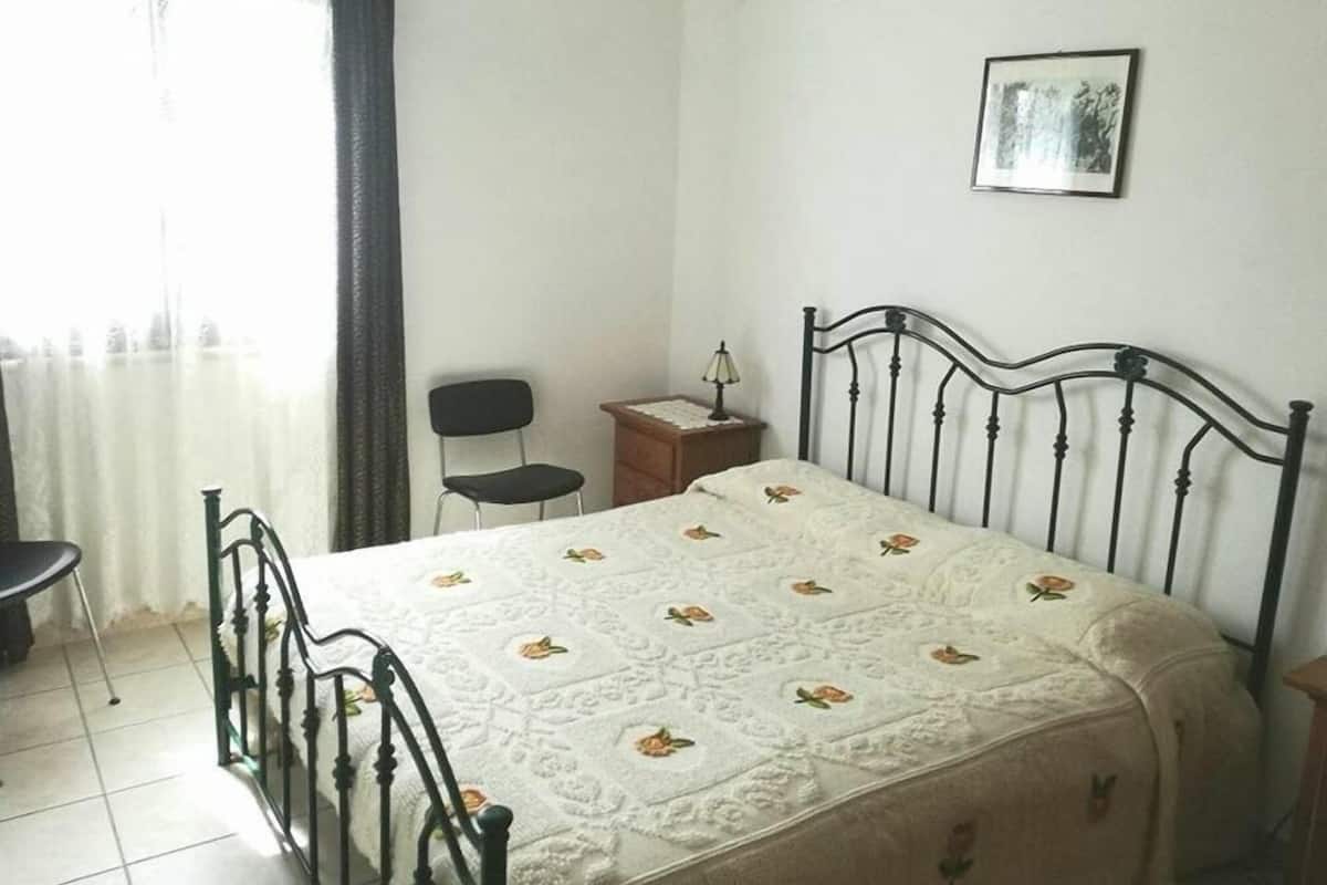 A bedroom with a bed, a chair, a nightstand, a lamp, and a picture on the wall.