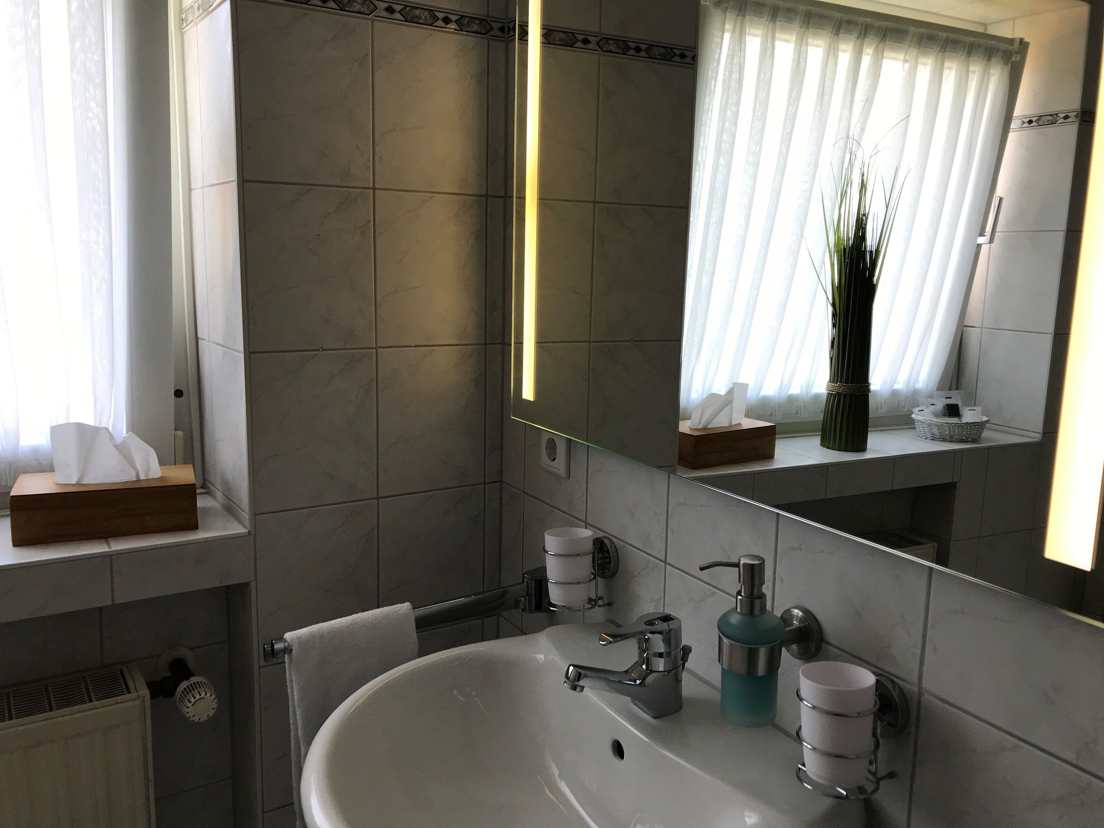 Un baño moderno con un lavamanos grande, un espejo y una ventana con cortinas.