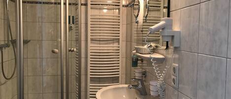 Un baño moderno con cabina de ducha de vidrio, toallero integrado, lavamanos con espejo y dispensador de toallas.