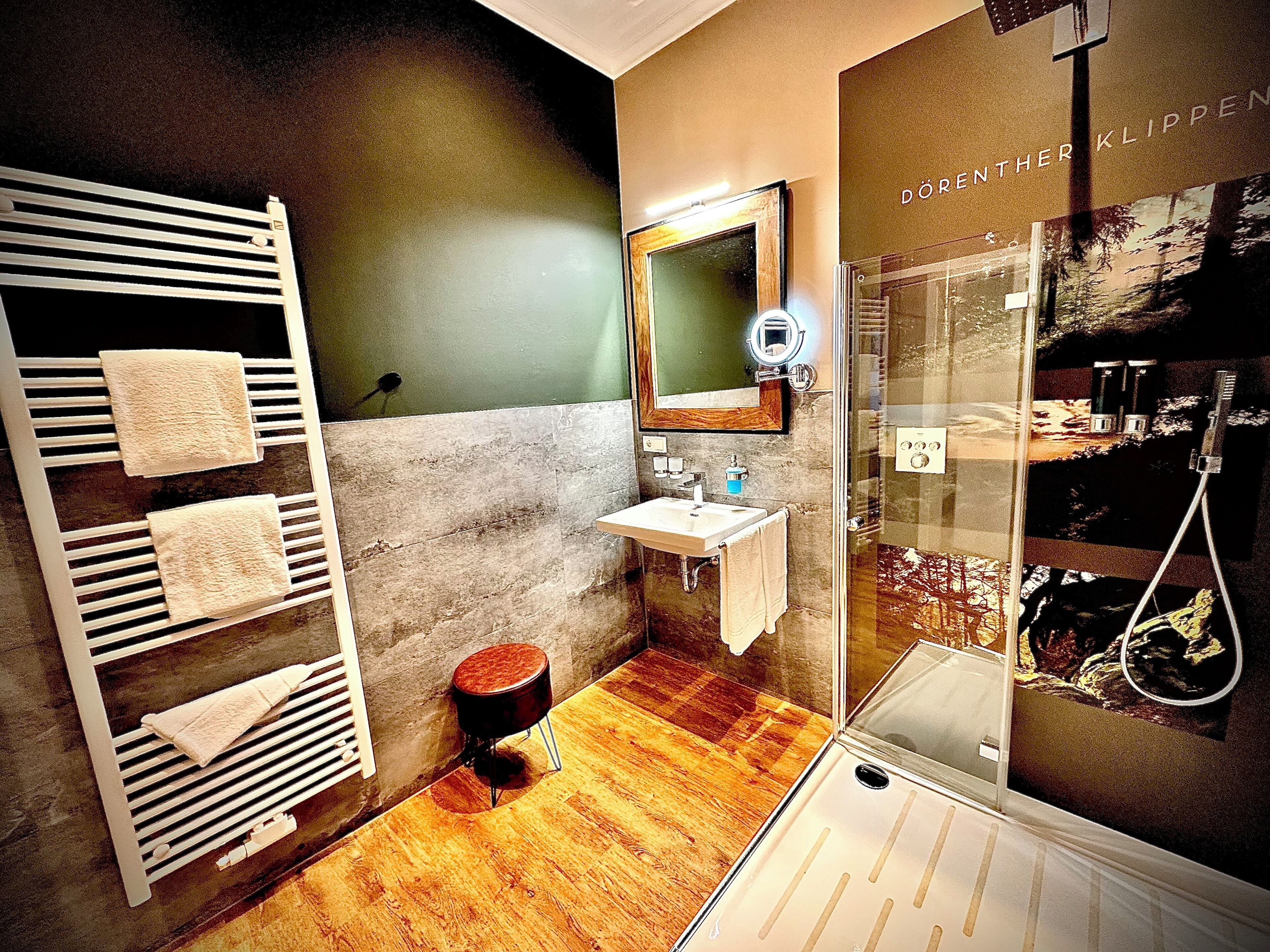 Une salle de bain moderne avec un plancher en bois, une cabine de douche en verre, un lavabo avec un miroir et un porte-serviettes.