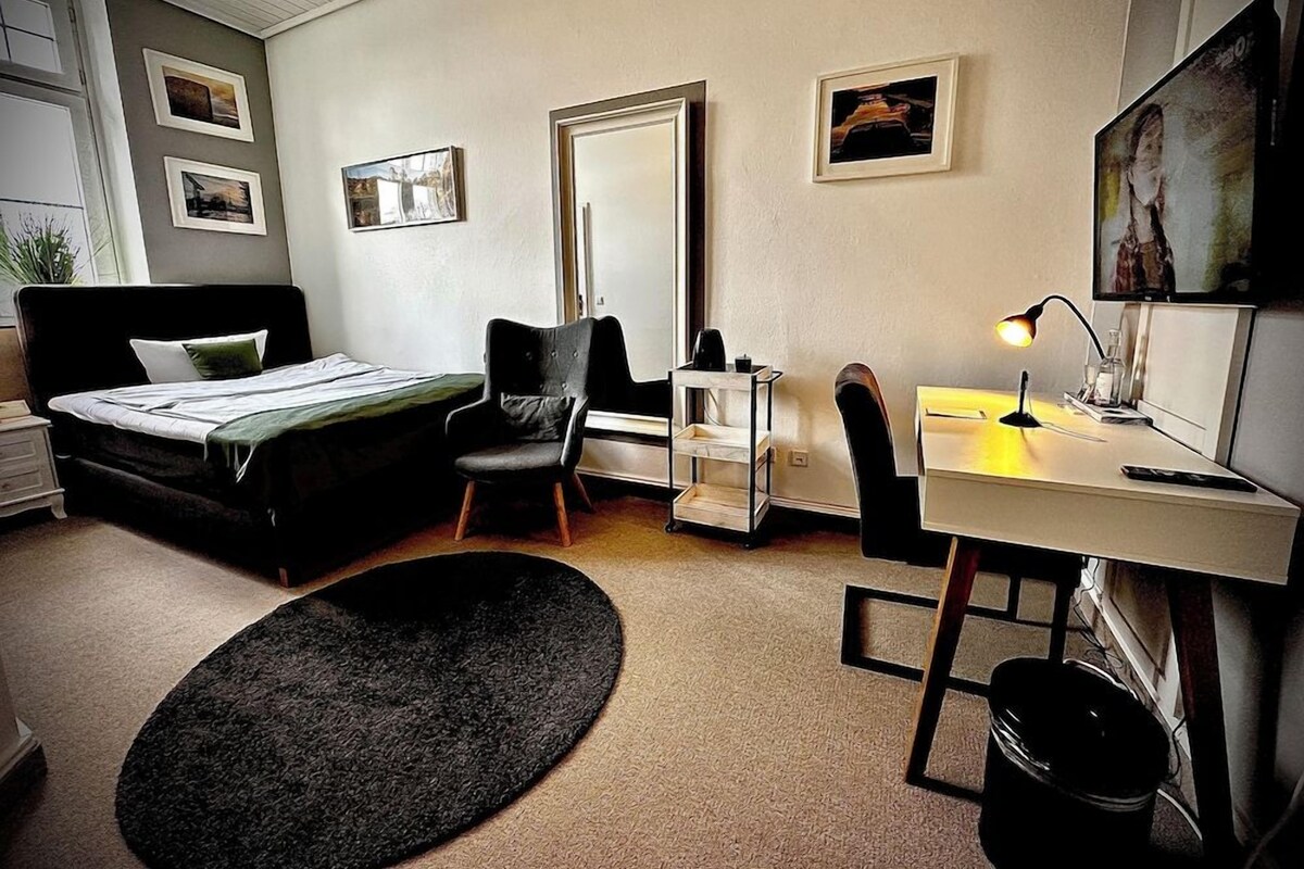 A bedroom with a bed, desk, chair, and a small rug.