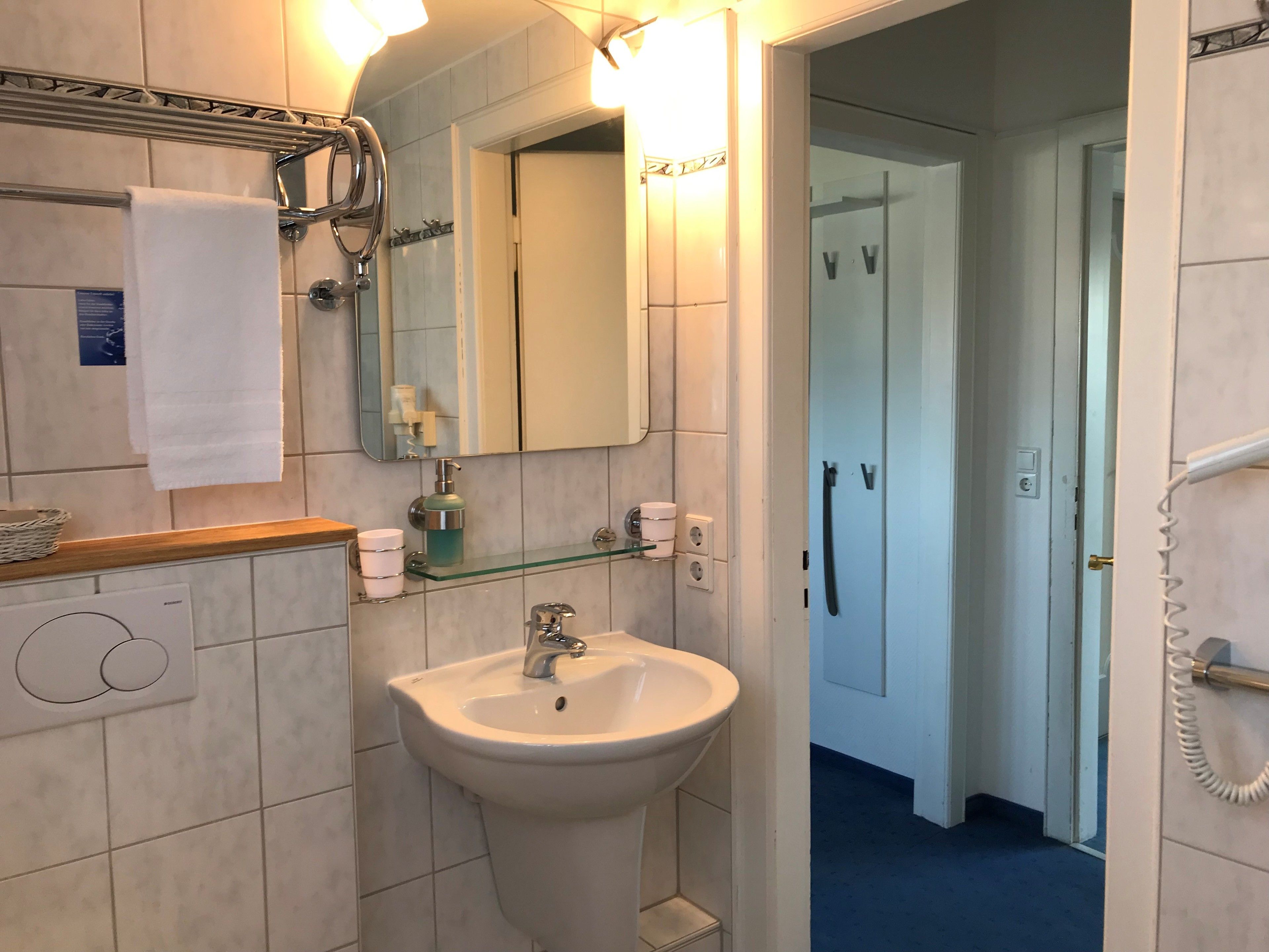 A bathroom with a sink, mirror, towel rack, and glass shelf with toiletries.
