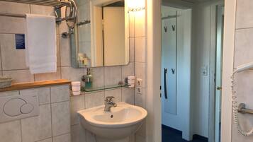 A bathroom with a sink, mirror, towel rack, and glass shelf with toiletries.