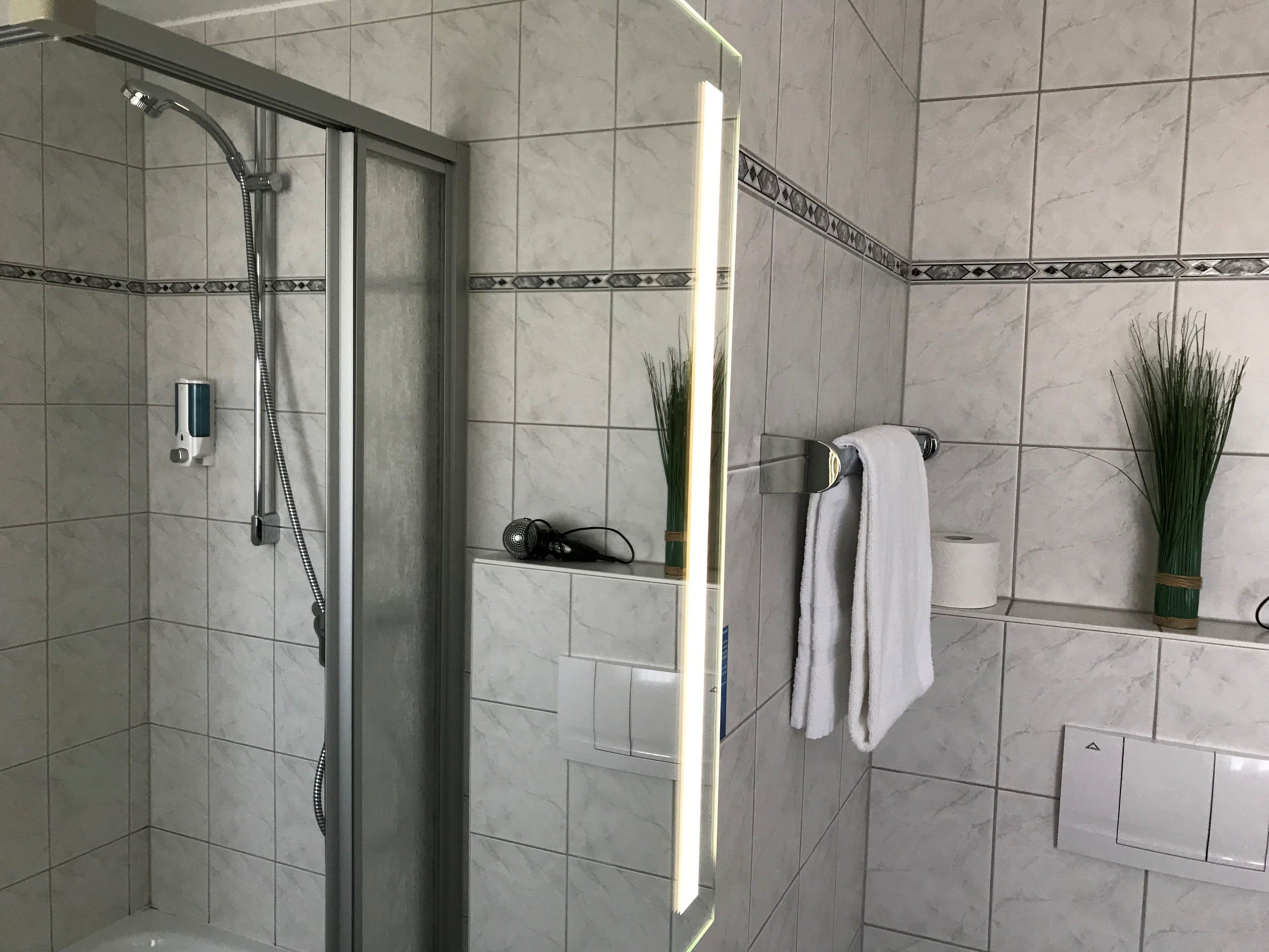 Un baño moderno con ducha envuelta en vidrio, un perchero y un estante con artículos de aseo.