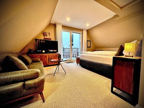 Una habitación de hotel con una cama grande, televisión, sofá y balcón con vistas.