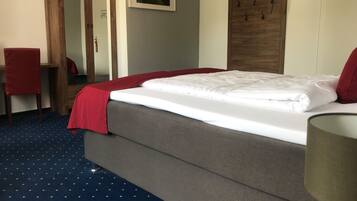 Una cama bien hecha con una colcha roja, un armario de madera, un espejo, una silla roja y una pequeña planta en maceta.