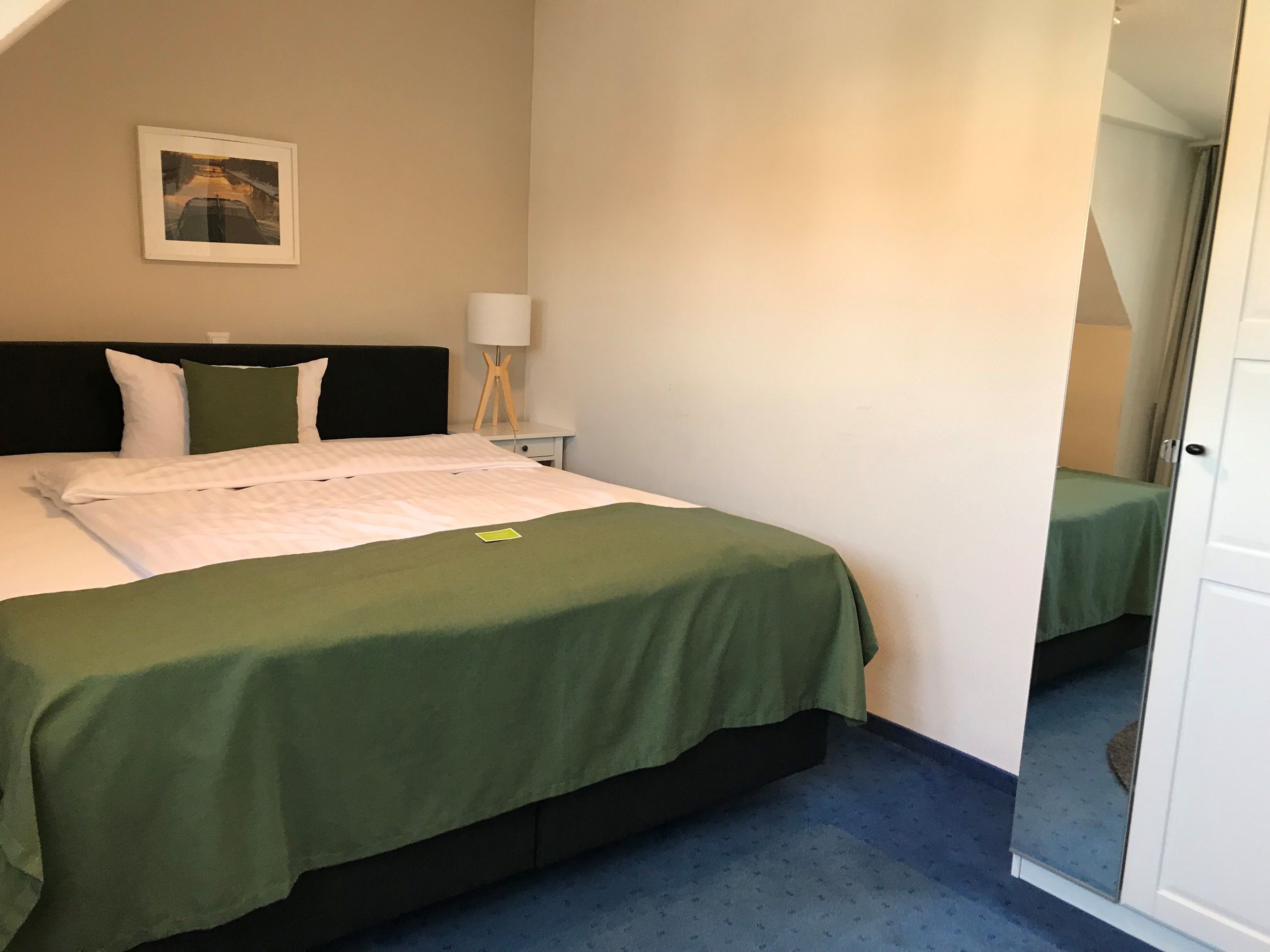A hotel room with a bed, a nightstand, a lamp, and a framed picture on the wall.