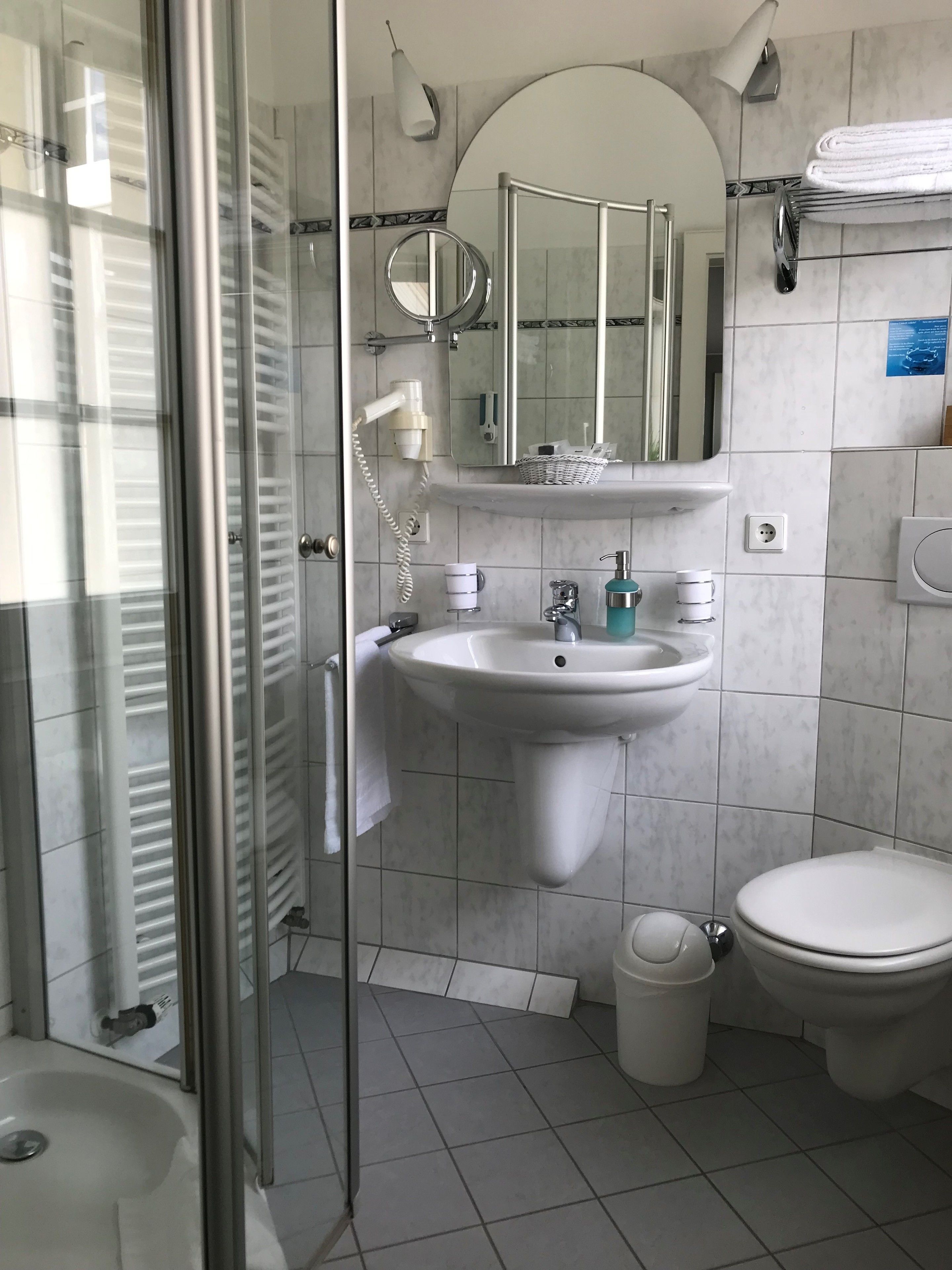 Ein modernes Badezimmer mit Duschkabine aus Glas, einem Standwaschbecken, einer Toilette und einem großen Spiegel über dem Waschbecken.