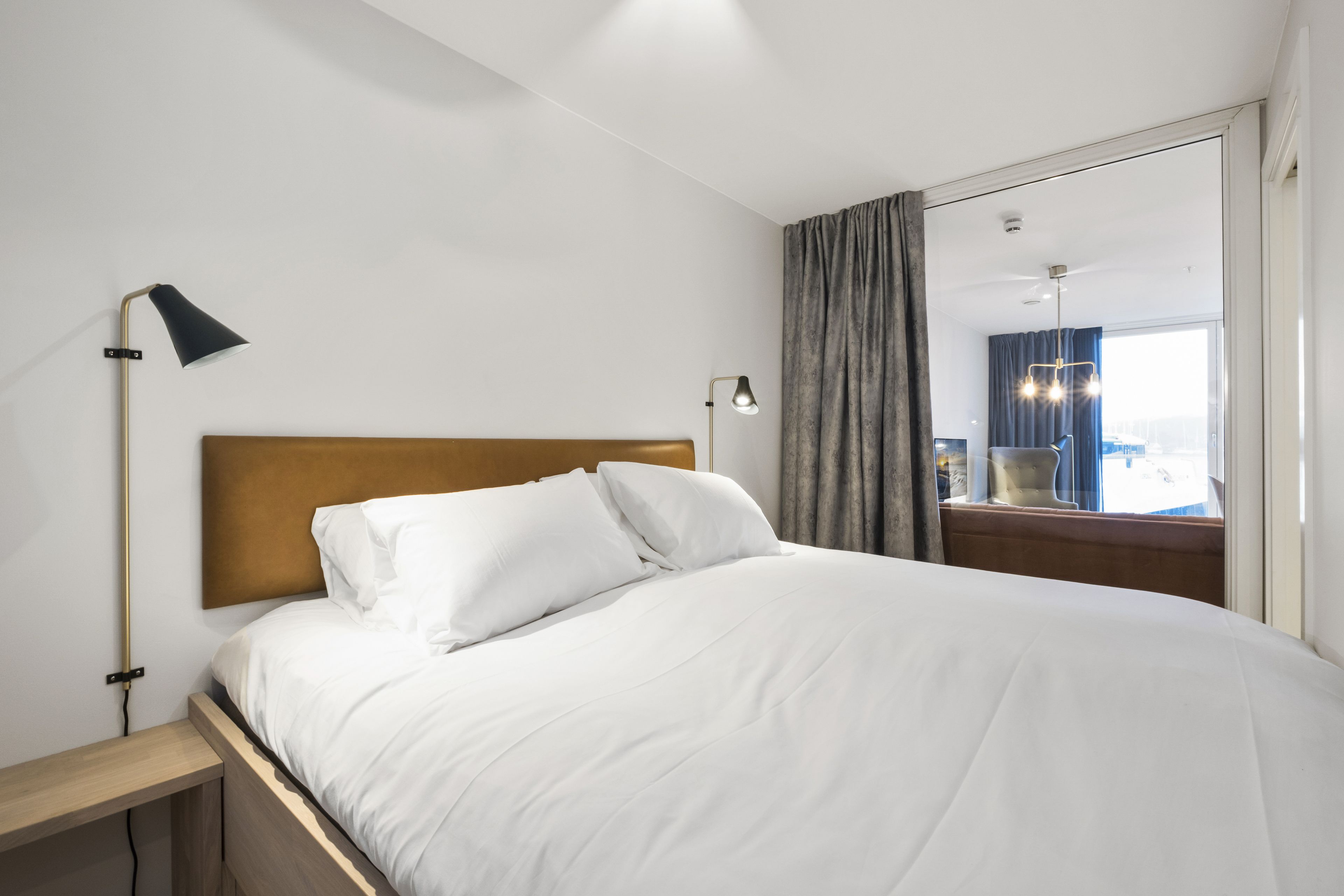 A neatly made bed with white linens, a wooden headboard, and two bedside lamps.