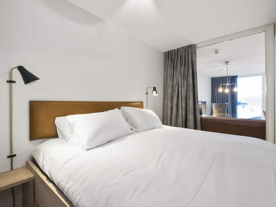 A neatly made bed with white linens, a wooden headboard, and two bedside lamps.
