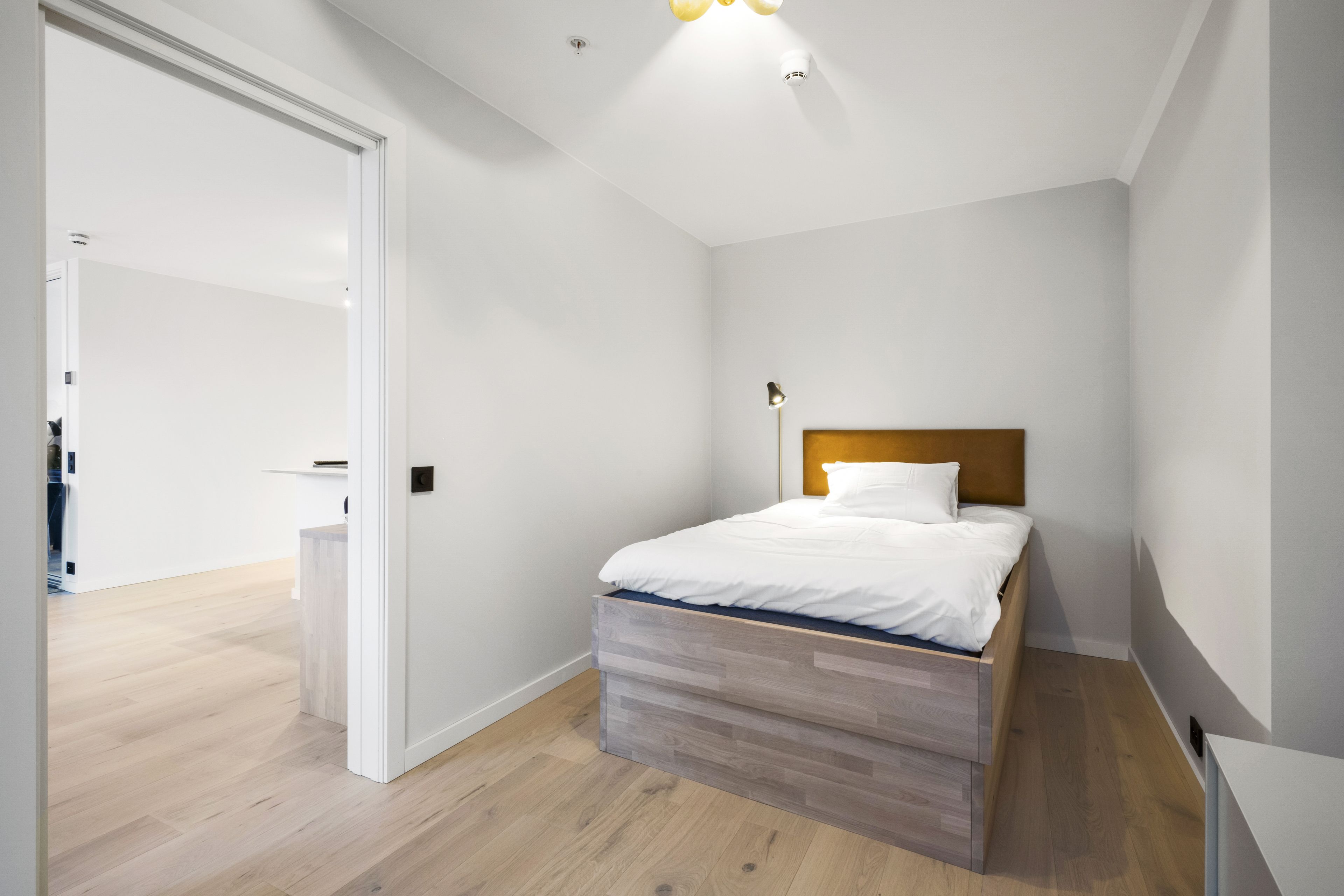 A bedroom with a wooden bed, white walls, and a wooden floor.
