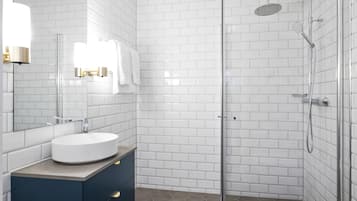 Un baño moderno con azulejos blancos tipo metro, un lavamanos redondo, armarios oscuros y una zona de ducha con mampara de vidrio.