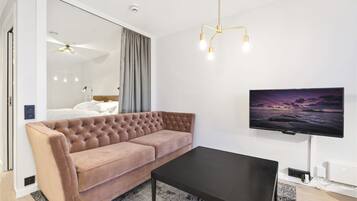 Un salon moderne avec un canapé capitonné, une table basse noire et un téléviseur fixé au mur qui diffuse une scène de coucher de soleil.