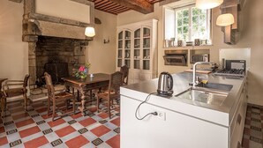 Une cuisine dotée d’une cheminée en pierre, d’une table à manger en bois et d’appareils électroménagers modernes.