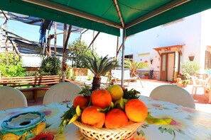 Una mesa con un cesto de naranjas y limones, una silla y un mantel con estampado floral.