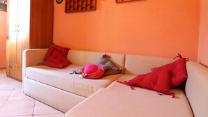 A beige sofa with red and gray cushions, a pink hat, and a wooden shelf with decorative items. - B&B La Maison De Titty & Margy (Piano di Sorrento)