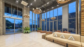 Un hall d’entrée spacieux avec un plafond haut, de grandes fenêtres et un espace salon moderne.