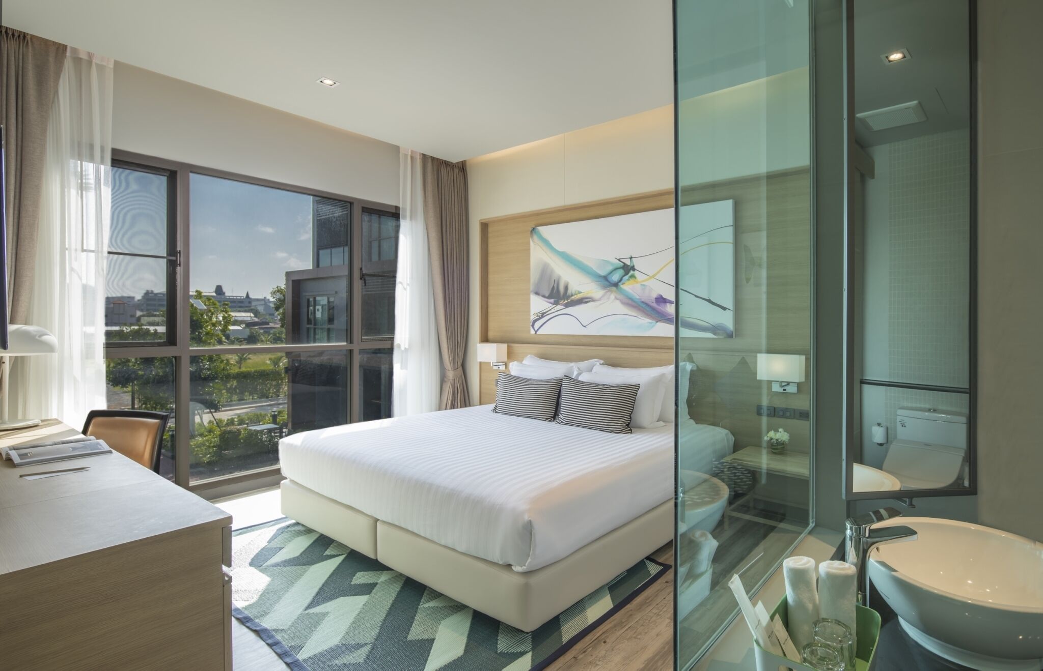 Habitación de hotel moderna con una cama grande, un escritorio, ducha con mampara de vidrio y vistas a la ciudad.