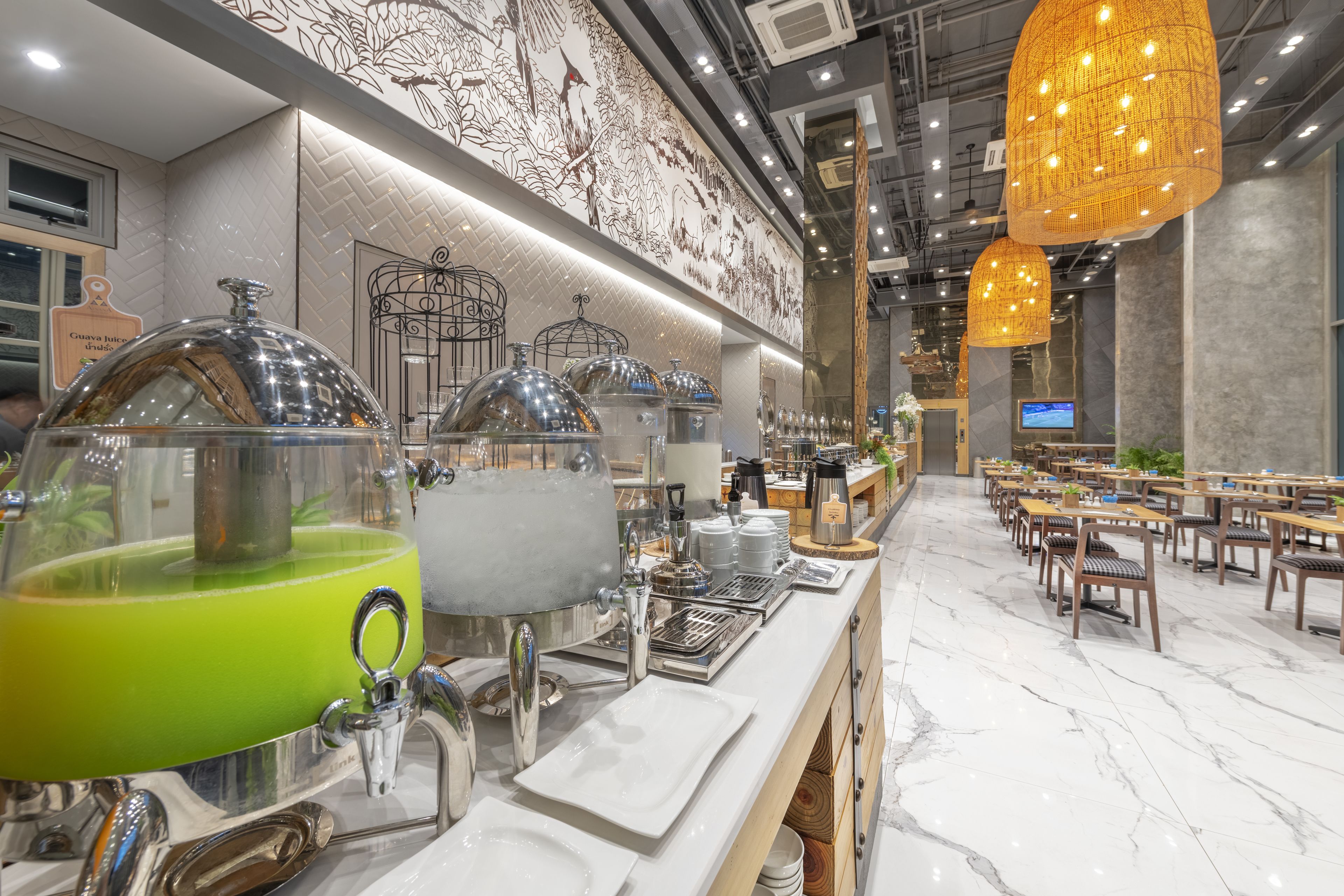 A buffet setup with a green drink dispenser, multiple serving stations, and a long counter with plates and utensils.