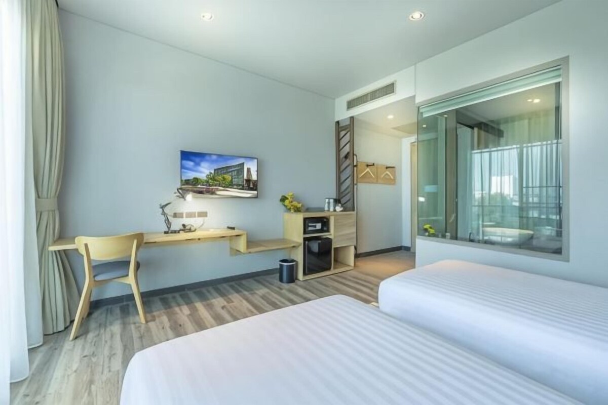 Habitació d'hotel amb llit, escriptori, cadira i una finestra gran.