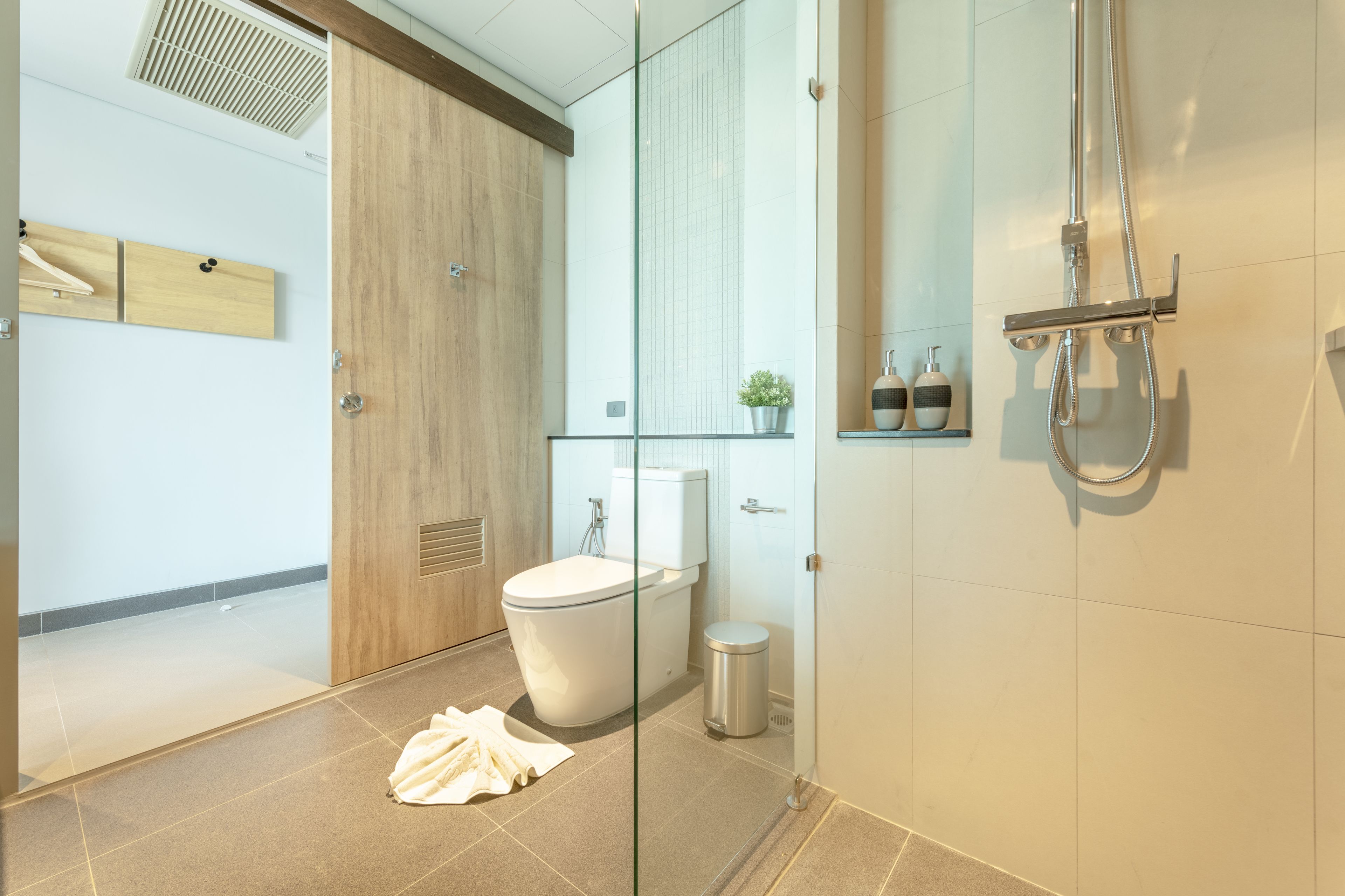 A modern bathroom with a glass shower enclosure, a toilet, and a small trash bin.