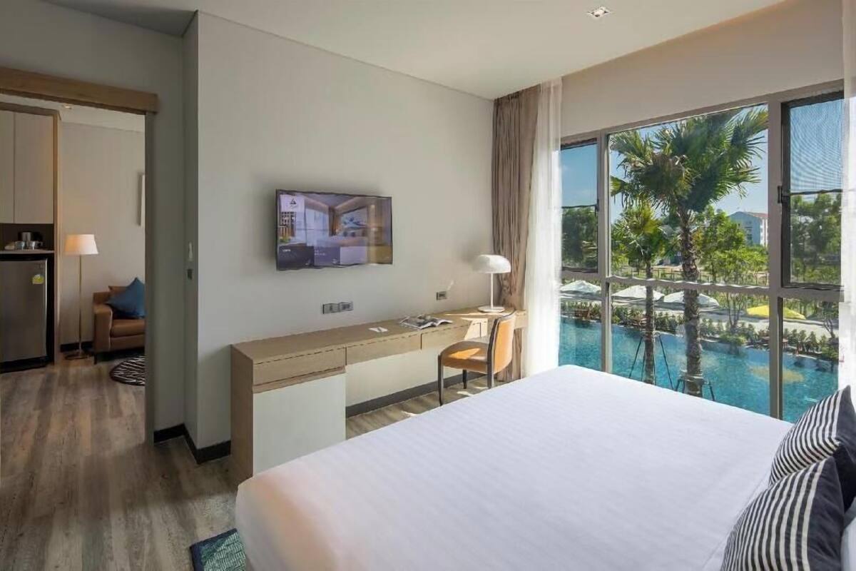 A hotel room with a bed, desk, chair, TV, and a view of a swimming pool.