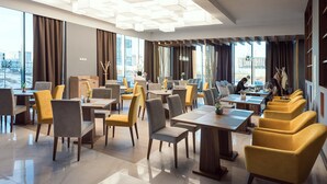 A modern hotel lobby with multiple seating areas, large windows offering city views, and a contemporary ceiling design.