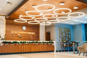 Un área de recepción con un mostrador de madera, luces de techo circulares, un reloj y un adorno en la pared.