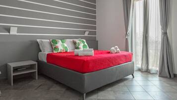 A modern bedroom with a grey bed, red bedding, and cactus-patterned pillows.