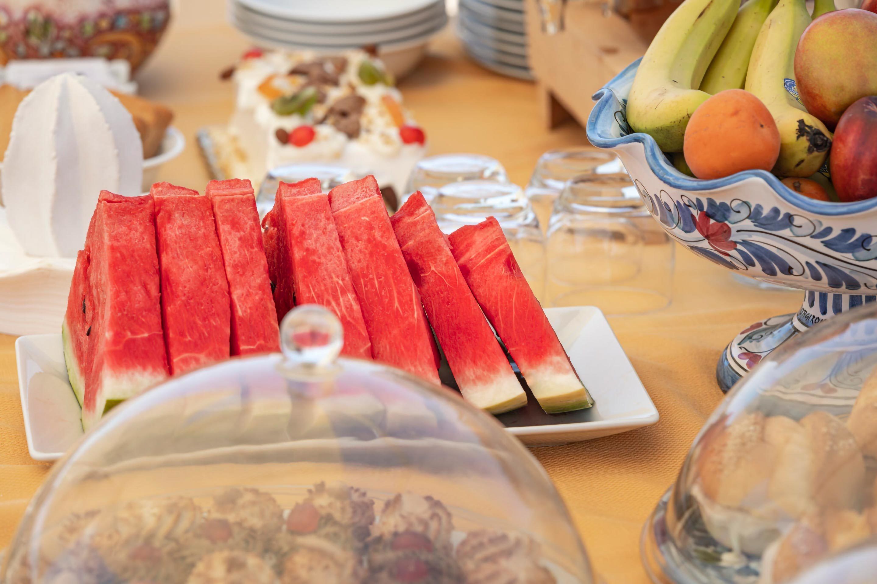 Ein Tisch mit verschiedenen Speisen, darunter Wassermelonenscheiben, eine Fruchtbowle und einem abgedeckten Gericht.