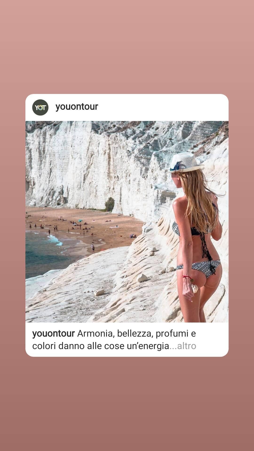 A person in a bikini standing on a cliff overlooking a beach with white cliffs in the background.