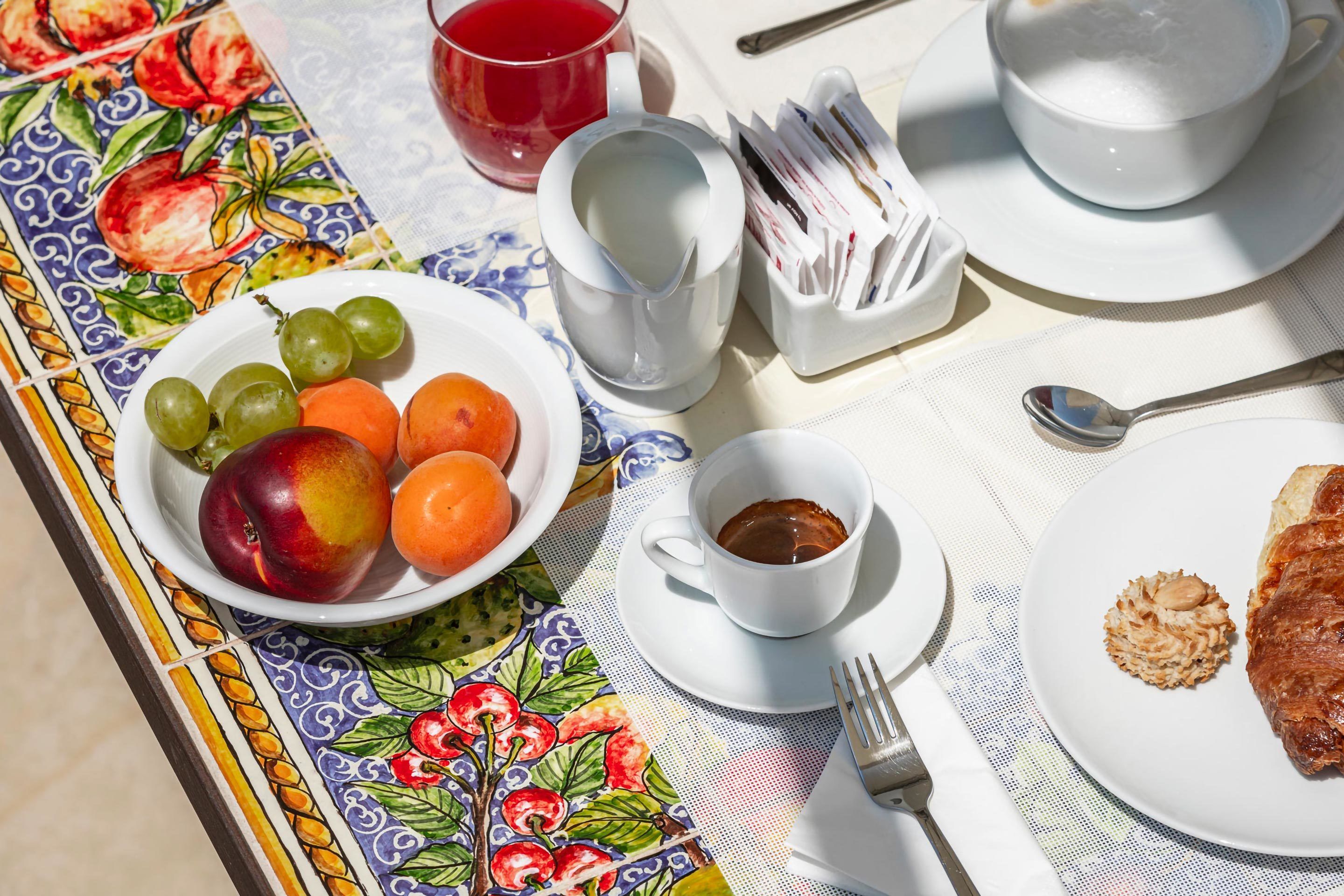 A table set with a plate of fruit, a cup of coffee, and a pastry.