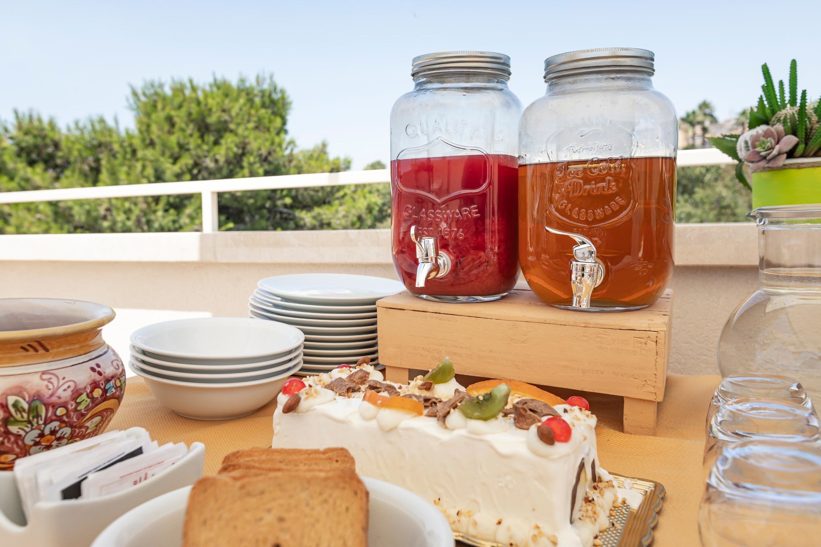 A table with a cake, two mason jars with drinks, and a potted plant.