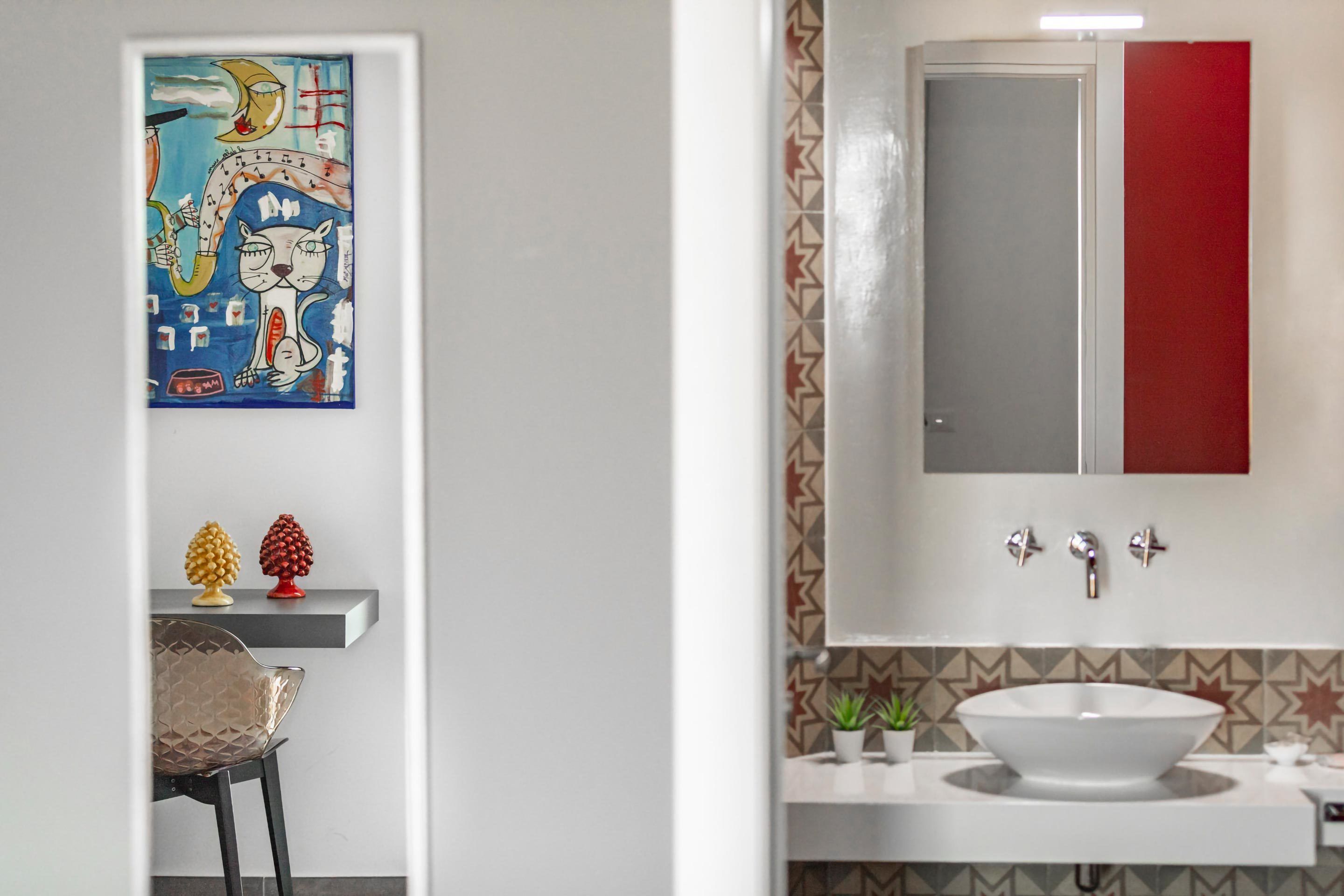 A bathroom with a white sink, a mirror, and a red cabinet.