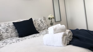 A neatly made bed with floral bedding, a black pillow, and a vase with white flowers. - Cosy One Bedroom Apartment By Creatick (Reading)